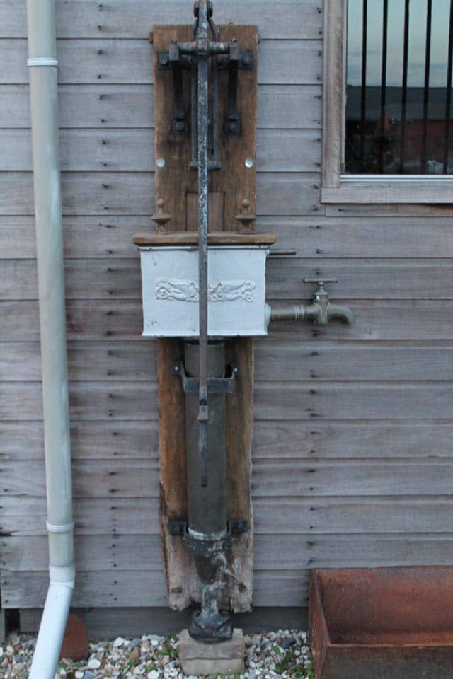 Zeer-mooie-unieke-waterpomp-met-mooie-bak-op-bord.-staat-bij-oude-zagerij